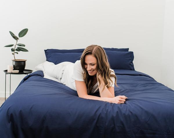 Woman in white laying across Haven Mattress with Nighttime Navy Blue bedding 